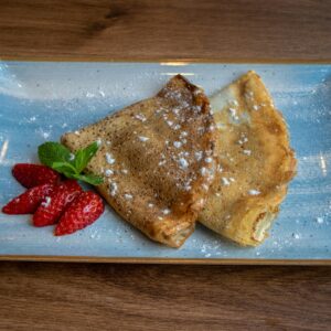 A plate of crêpes dusted with powdered sugar, served with strawberries and mint.