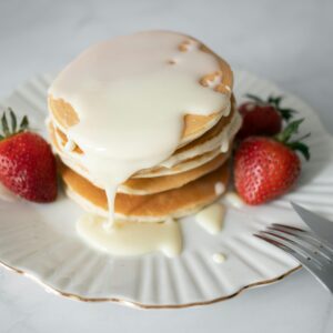 Delicious pancakes topped with cream and fresh strawberries on a plate.
